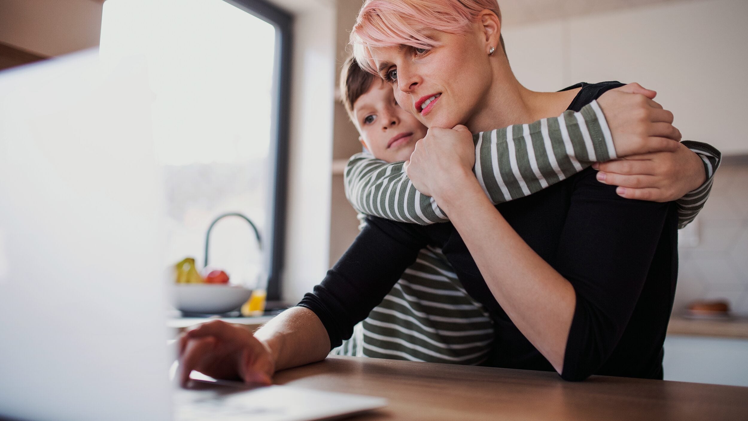 Woman with young child works on a laptop at home.