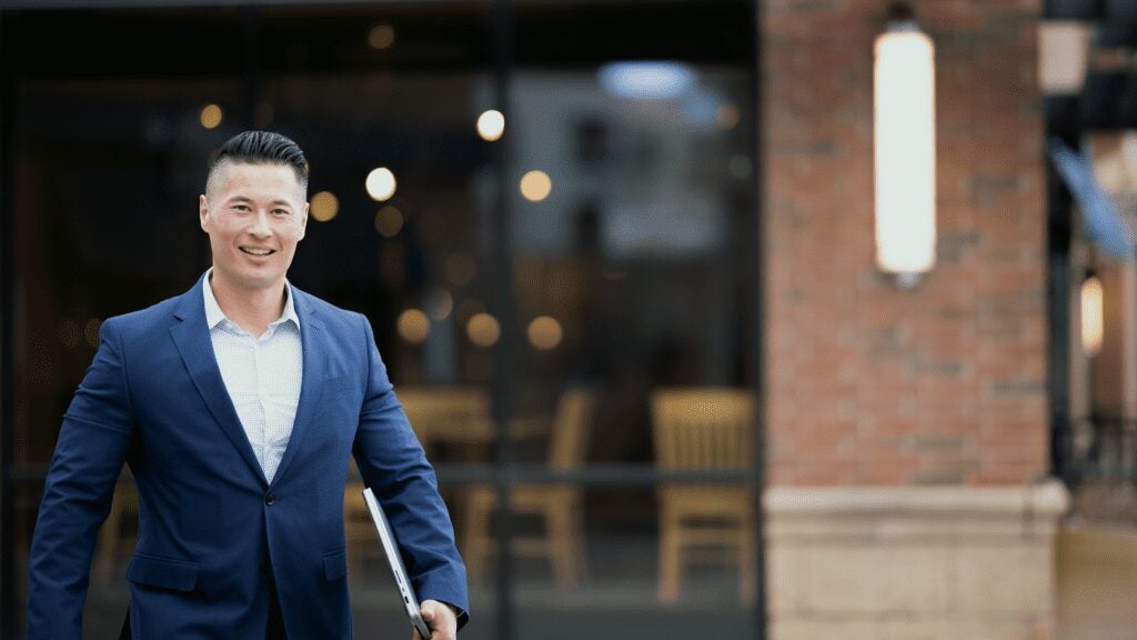 Man carrying laptop walks outside of his workplace.